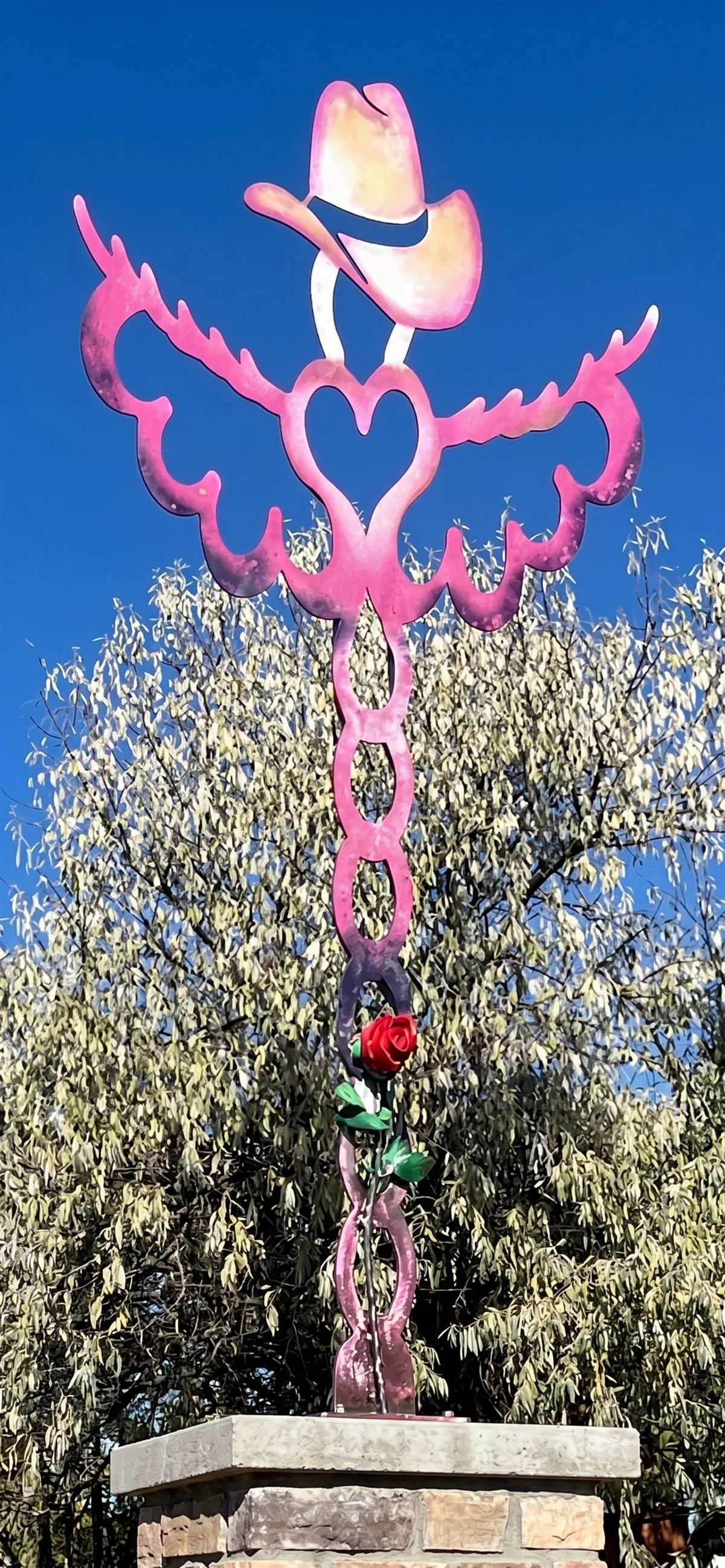 Vibrant pink metal angel monument with a cowboy hat and heart